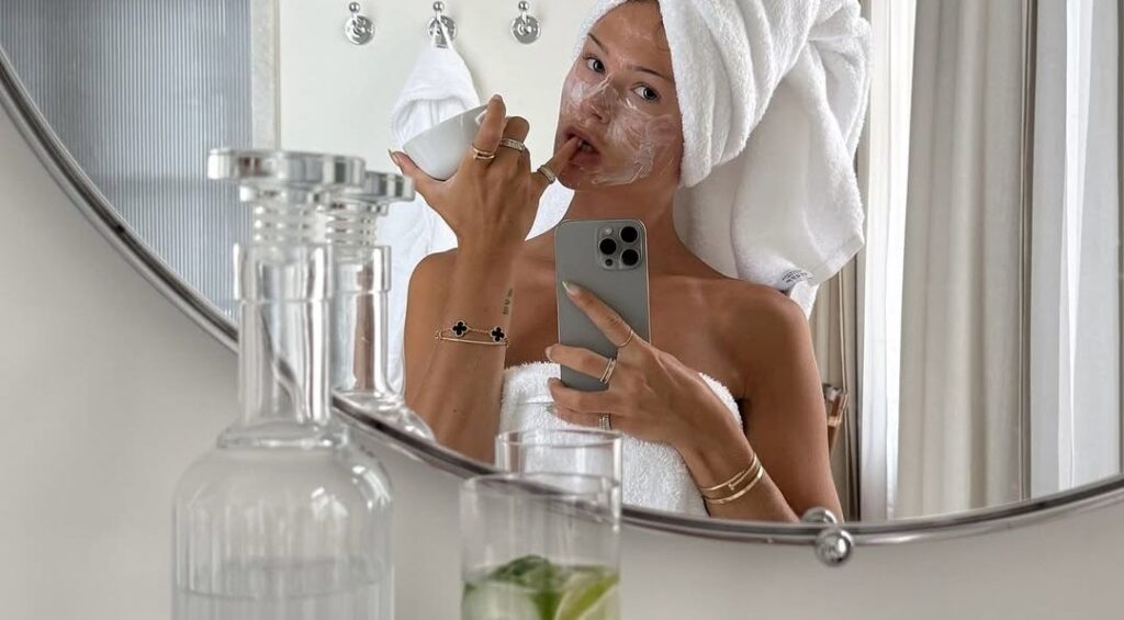 "Pampering rainy day self-care routine applying a face mask while wearing a plush towel"