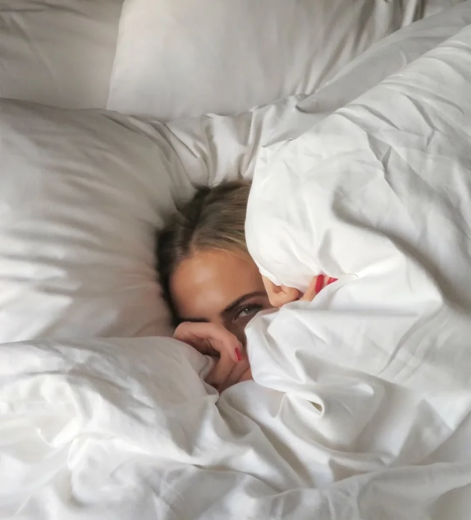 "Woman with red nails peeking out from under a cozy white duvet"